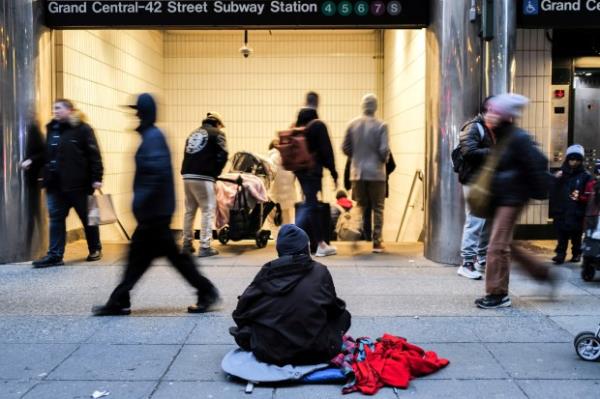 People walk past a homeless man sitting on the sidewalk in the Manhattan borough of New York on January 29, 2024. (Photo by CHARLY TRIBALLEAU/AFP via Getty Images)