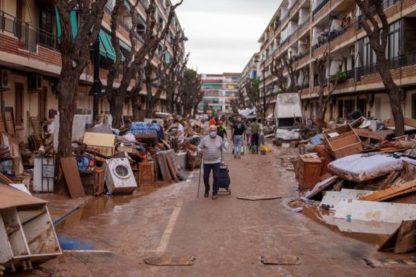 People walk through a street with piled furniture and rubbish on the sides, in an area affected by floods in Benetusser, Spain, on Nov. 4, 2024.