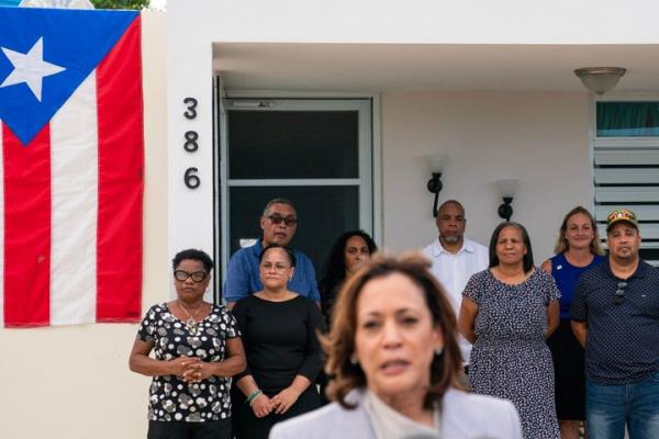 Residents watch from their porch as Vice President Kamala Harris speaks after touring a private home in Canovanas, Puerto Rico, on March 22, 2024.