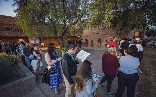 US voters lining up to cast their ballots in person read voting guides handed out by volunteers at the Fowler School polling station in Tempe, Arizona, on the country's Election Day, 5 November, 2024.