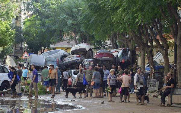 Residents gather in the street next to a pile of cars on October 31, 2024 after flash floods affected the town of Massanassa, in the region of Valencia, eastern Spain. - Rescuers raced on October 31, 2024 to find survivors and victims of once-in-a-generation floods in Spain that killed at least 95 people and left towns submerged in a muddy deluge with overturned cars scattered in the streets. a<em></em>bout 1,000 troops joined police and firefighters in the grim search for bodies in the Valencia region as Spain started three days of mourning. Up to a year's rain fell in a few hours on the eastern city of Valencia and surrounding region on October 29 sending torrents of water and mud through towns and cities. (Photo by JOSE JORDAN / AFP)