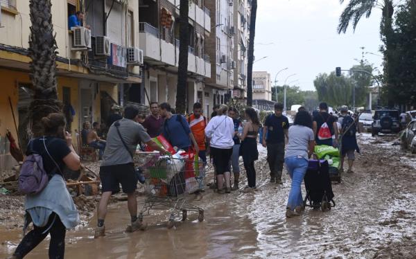 People push shopping carts along a street covered in mud on October 31, 2024 after flash floods ravaged Paiporta, in Valencia, eastern Spain. - Rescuers raced on October 31, 2024 to find survivors and victims of once-in-a-generation floods in Spain that killed at least 95 people and left towns submerged in a muddy deluge with overturned cars scattered in the streets. a<em></em>bout 1,000 troops joined police and firefighters in the grim search for bodies in the Valencia region as Spain started three days of mourning. Up to a year's rain fell in a few hours on the eastern city of Valencia and surrounding region on October 29 sending torrents of water and mud through towns and cities. (Photo by JOSE JORDAN / AFP)