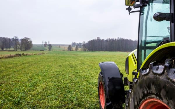 Rainy day in late autumn. Tractor on the edge of a meadow with green grass. Forest in the background. Podlasie, Poland.