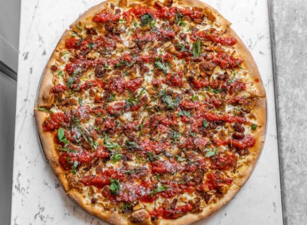 a slice of pizza with burratta and fresh basil on a wood table.