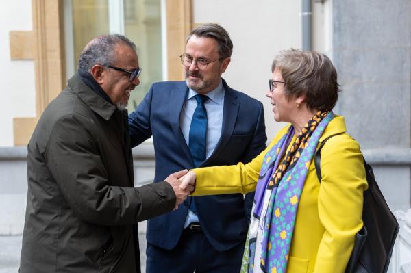 Two men and a woman are greeting each other by shaking hands and smiling.